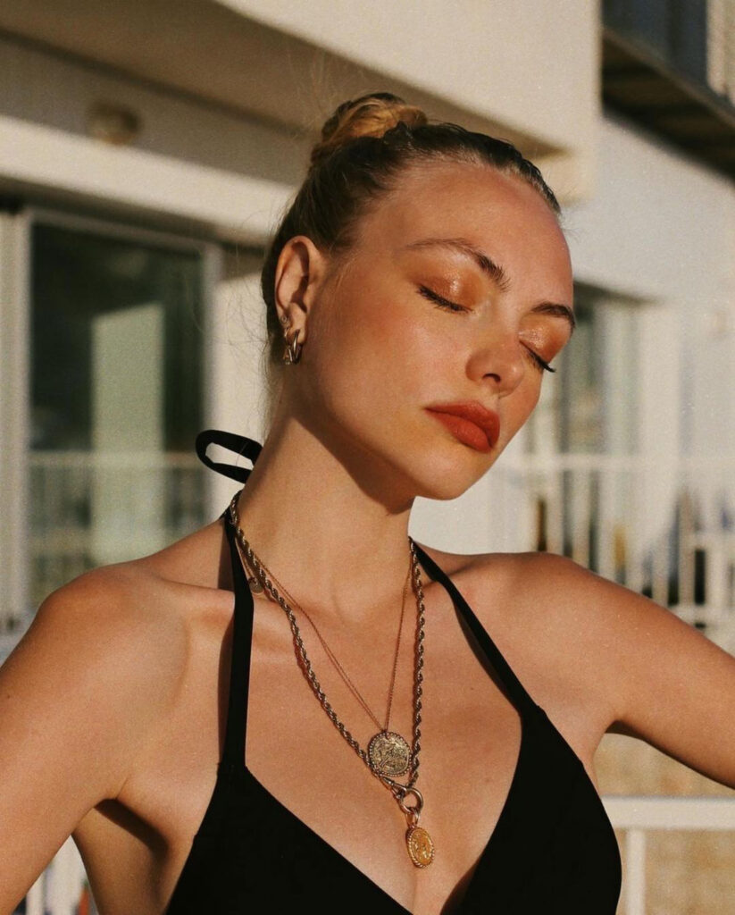 Femme en maillot de bain noir avec colliers dorés, lumière dorée sur peau bronzée, portrait mode à Marseille par WoW Agency, agence marketing digital. Pain de Sucre